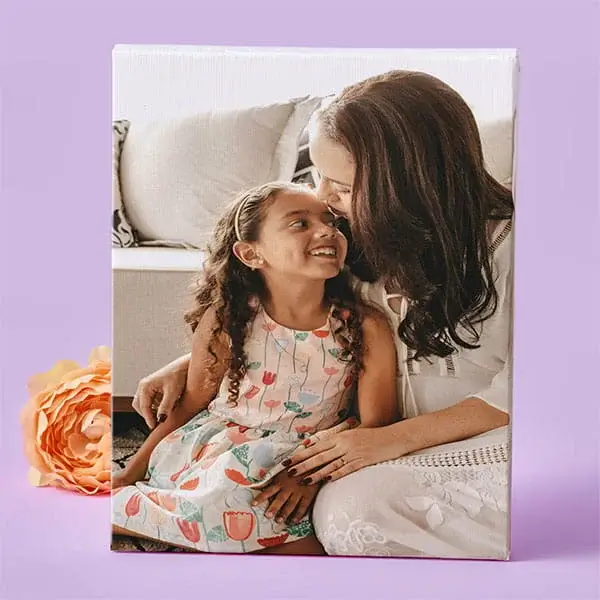 A canvas print featuring a woman and a young girl sitting together on a sofa, sharing a warm and affectionate moment, with a peach flower placed beside the frame.